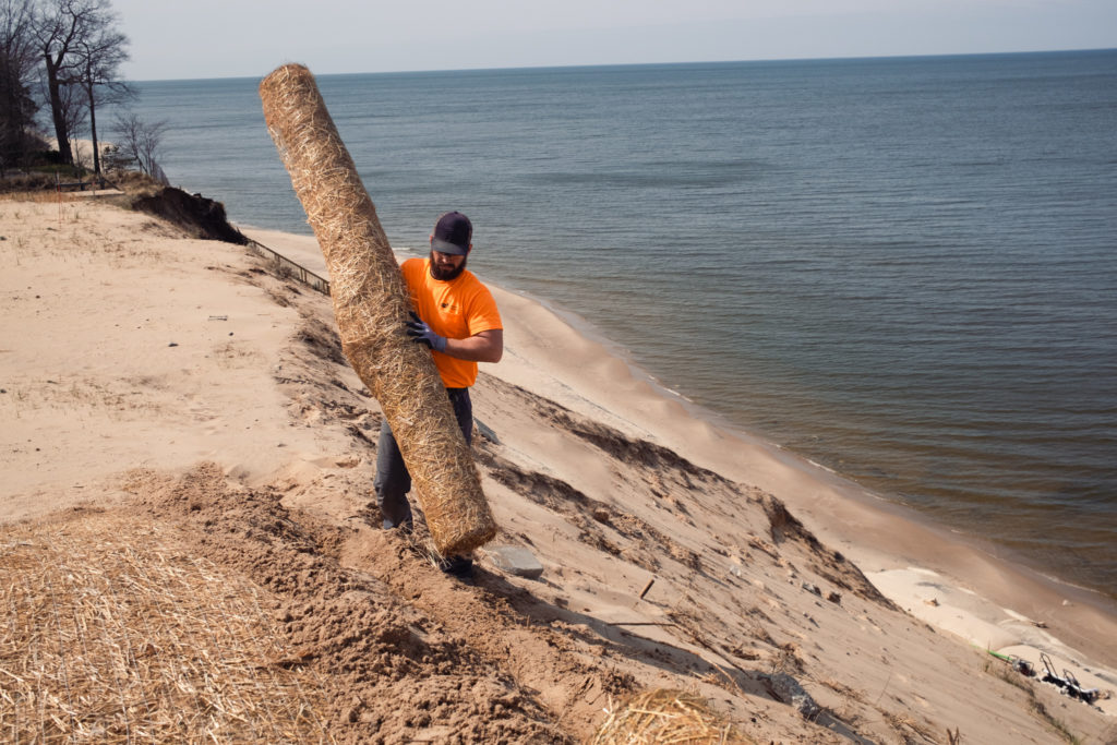 Worker carrying straw mat to side of sand dune with lake in background