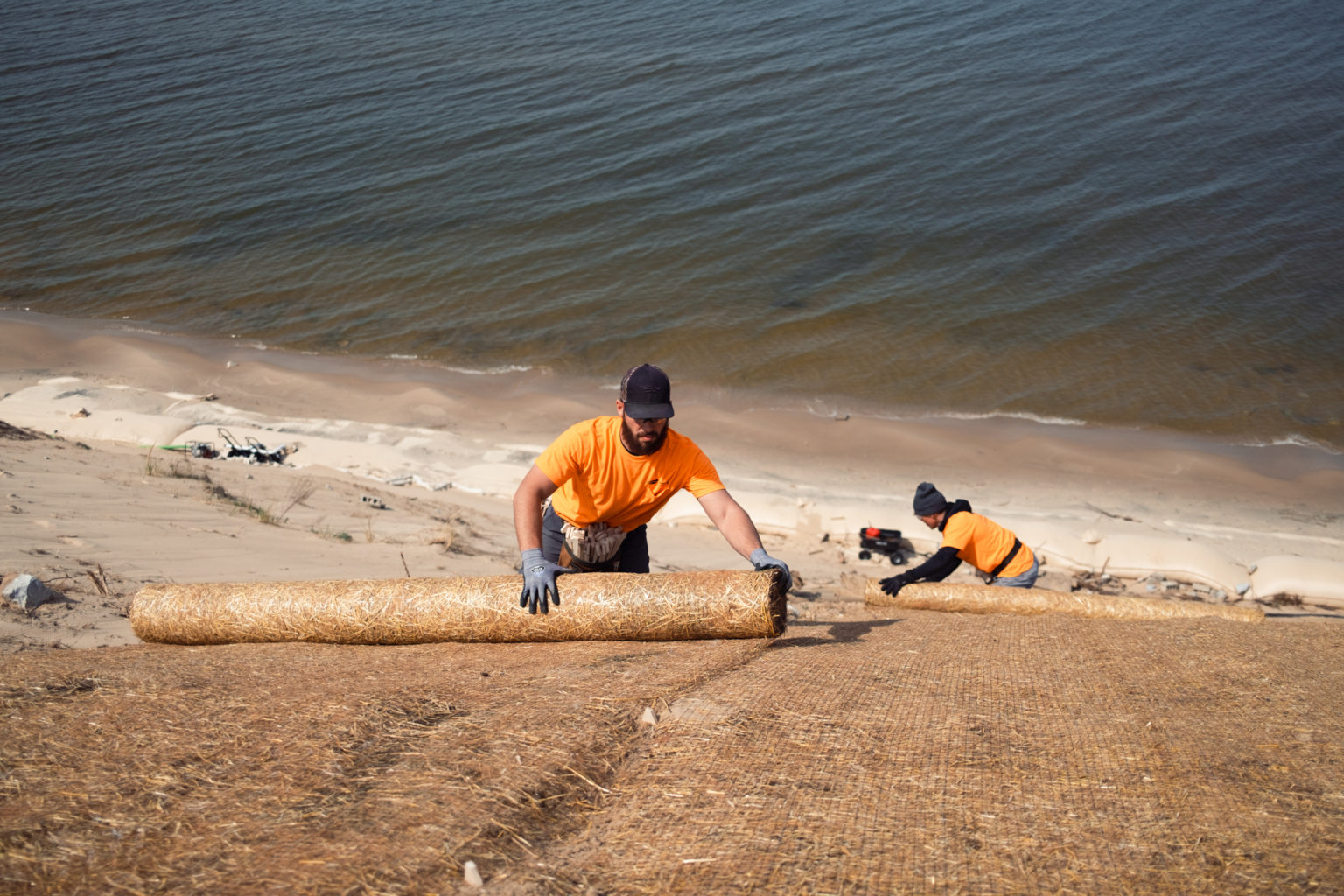 To workers laying out straw mat with lake in background