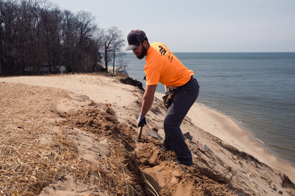 A Lakeshore Customs employee uses a shovel to dig a trench at the top of the dune.
