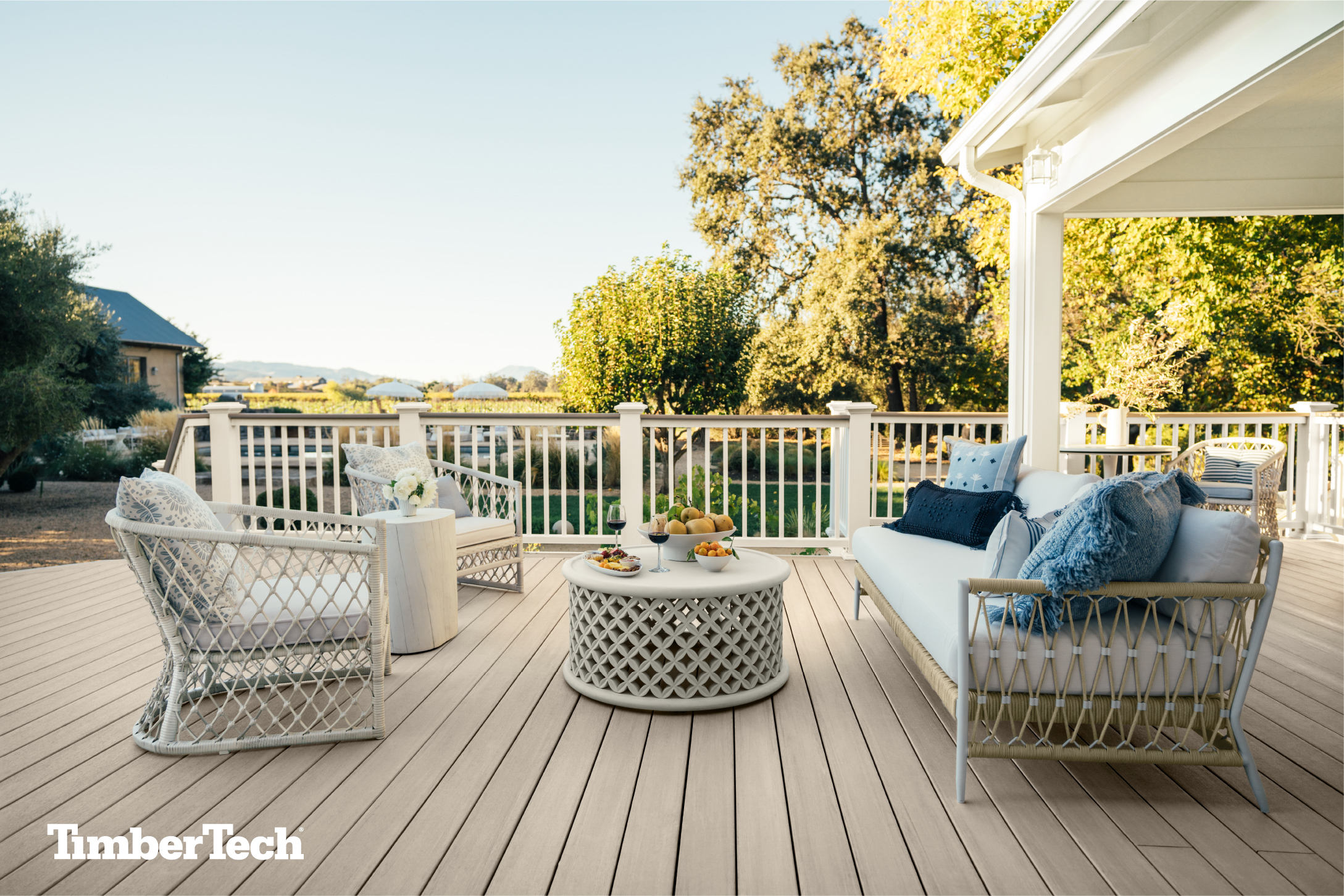A finished, light-colored TimberTech deck decorated with white patio furniture.