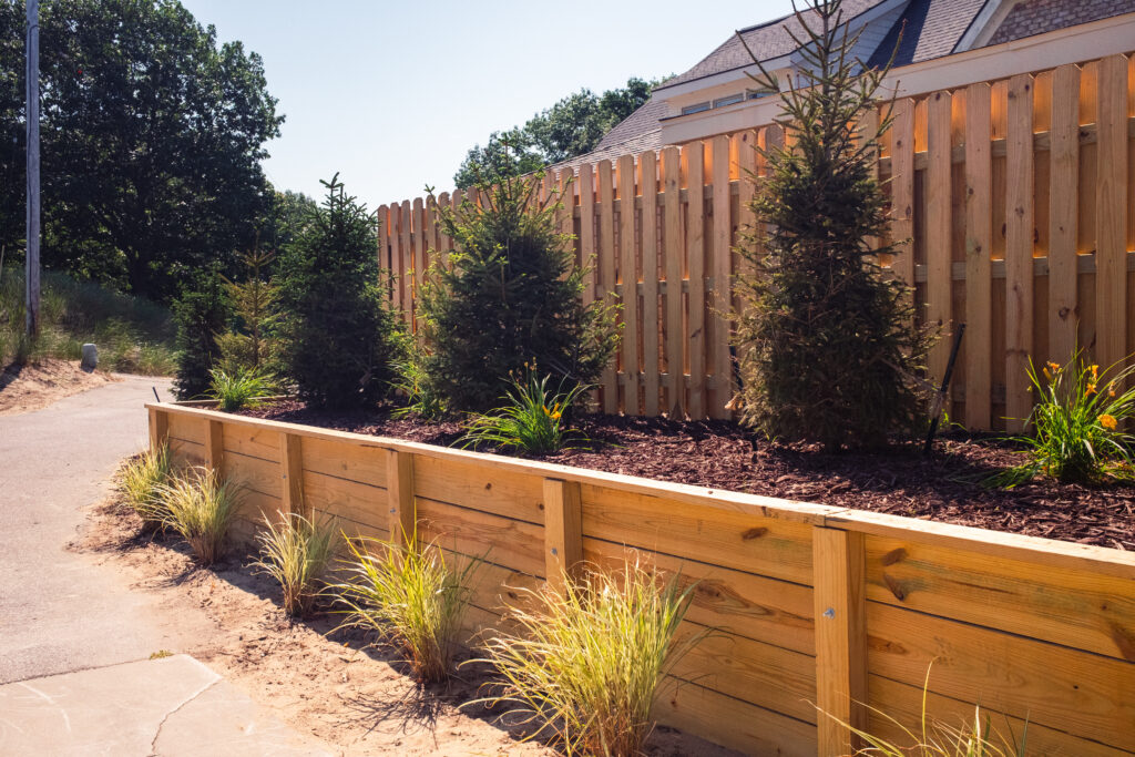 A lakefront property's natural landscaping with a wood retaining wall, beach grass, and pine trees.